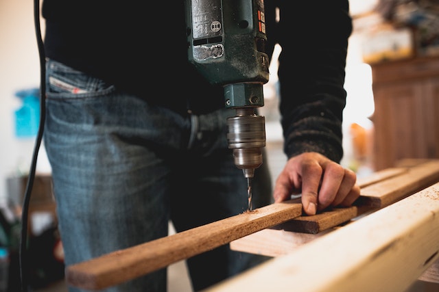 repair-person-using-drill-on-wood